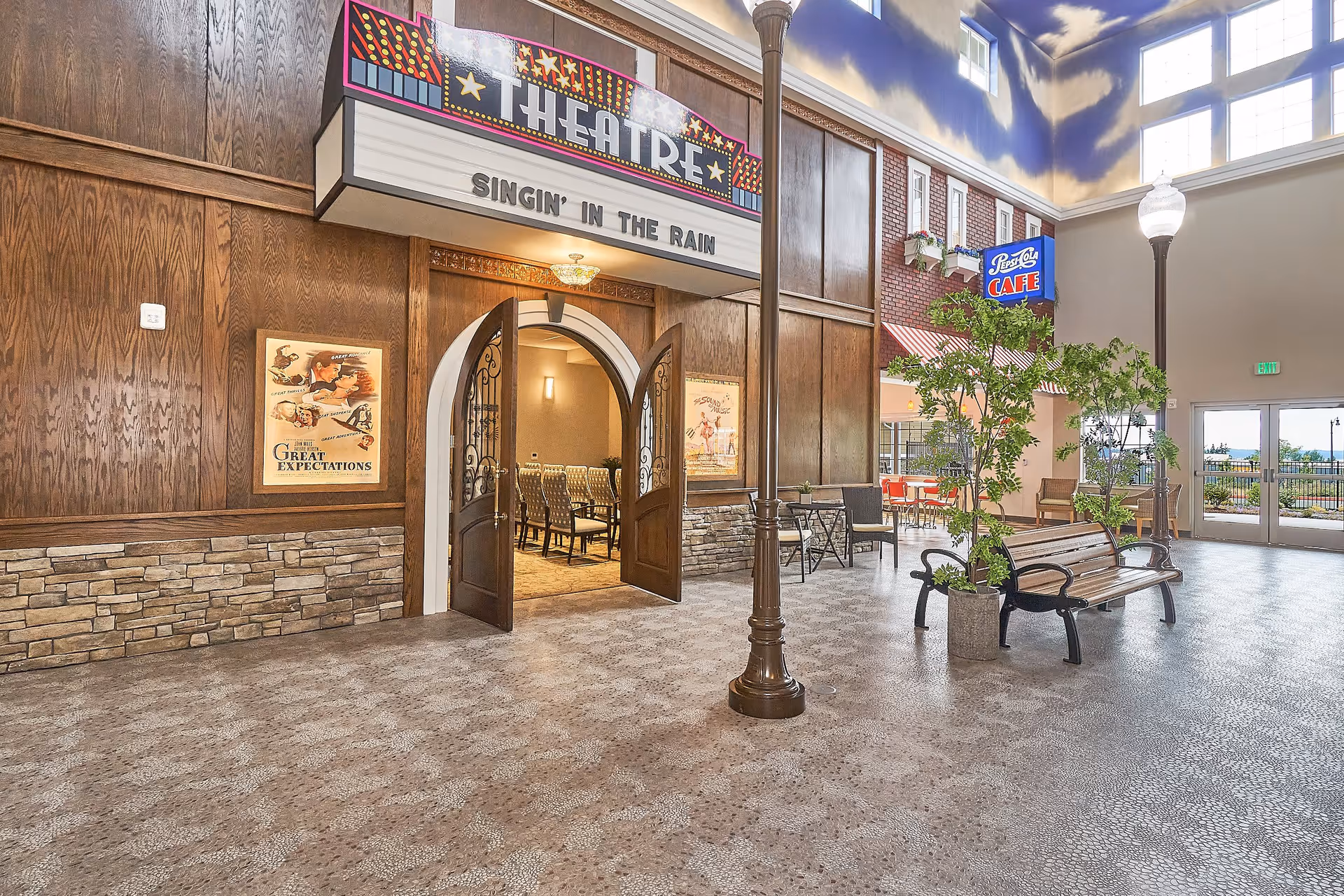 Spacious indoor lobby styled like a small-town street with a theatre marquee, benches, lamp posts, and café seating.