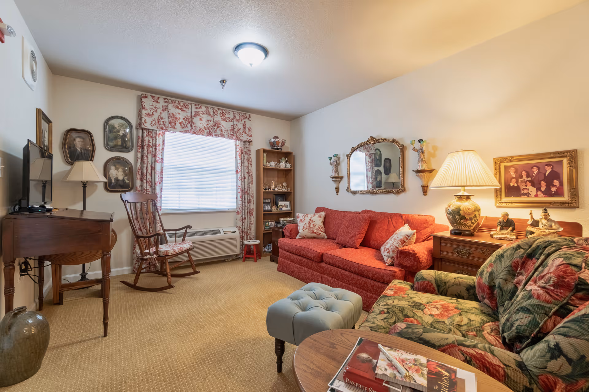 Cozy living room with a red sofa, floral armchair, rocking chair, side tables, and decorative wall art.