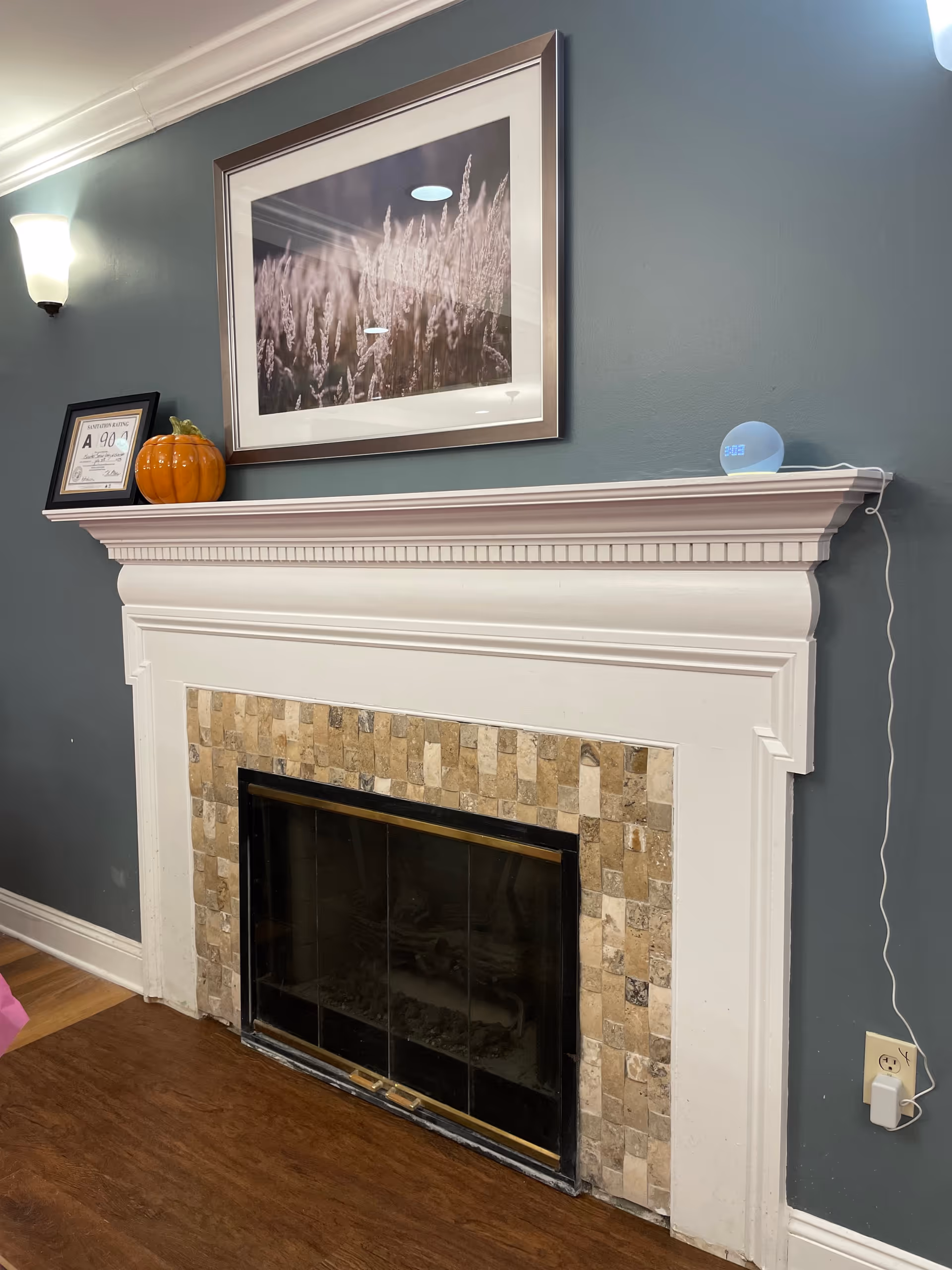 White fireplace mantel with tile surround, framed artwork above and small decorative items on the mantel in a living room.