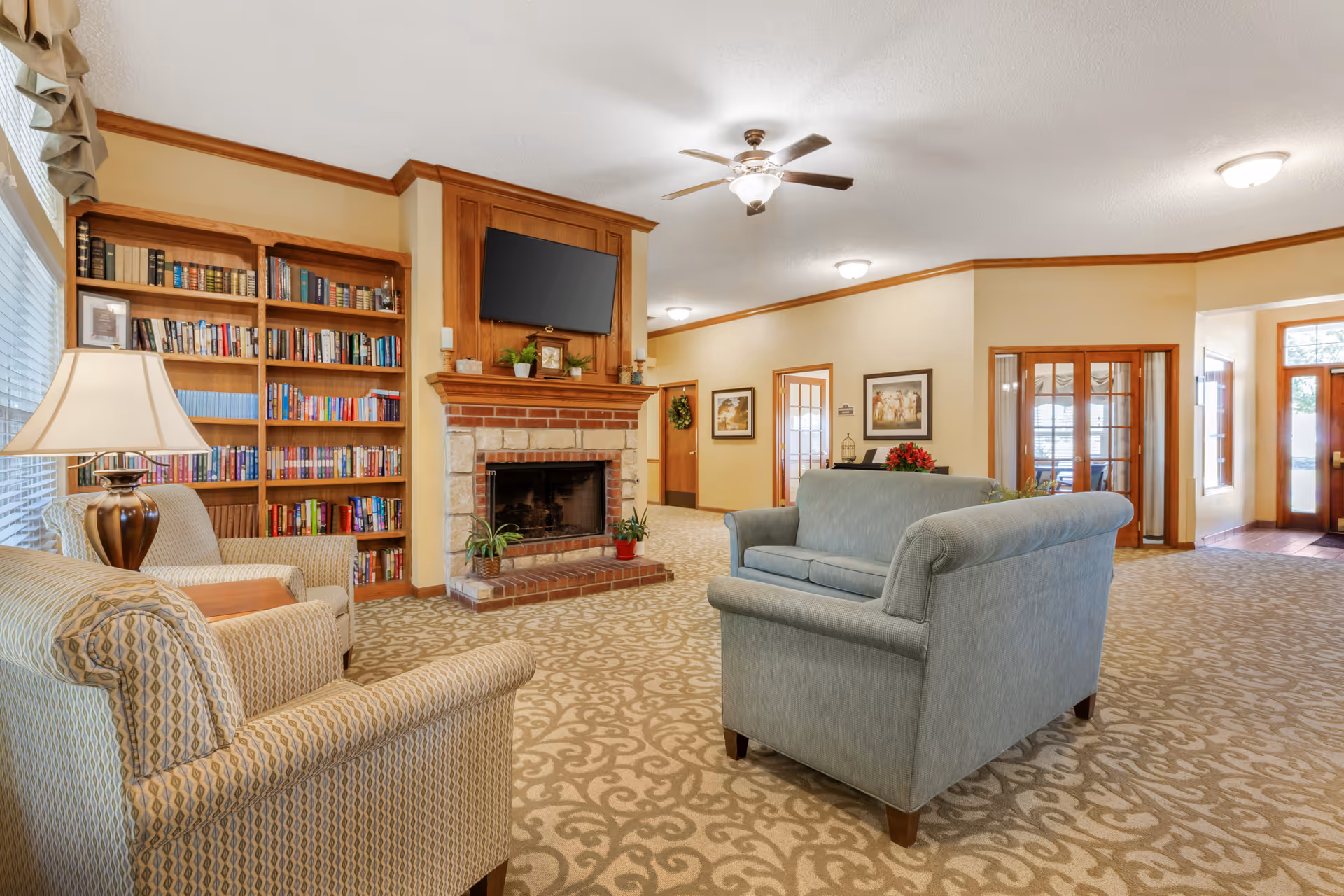 Cozy communal living room with sofas, armchairs, a fireplace, built-in bookshelves, and a wall-mounted TV.