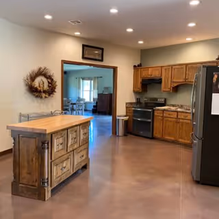 Open kitchen with wooden cabinets, stainless steel appliances, a central wooden island, and an adjacent dining area visible through a doorway.