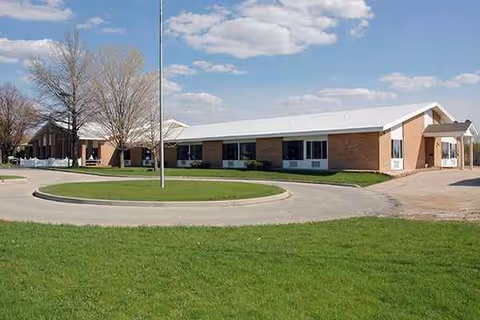 Brick senior living facility with a circular driveway and manicured lawn in front.