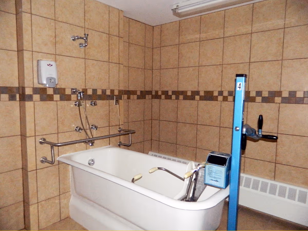 Tiled bathroom with a freestanding bathtub fitted with grab bars and a blue mechanical lift device.