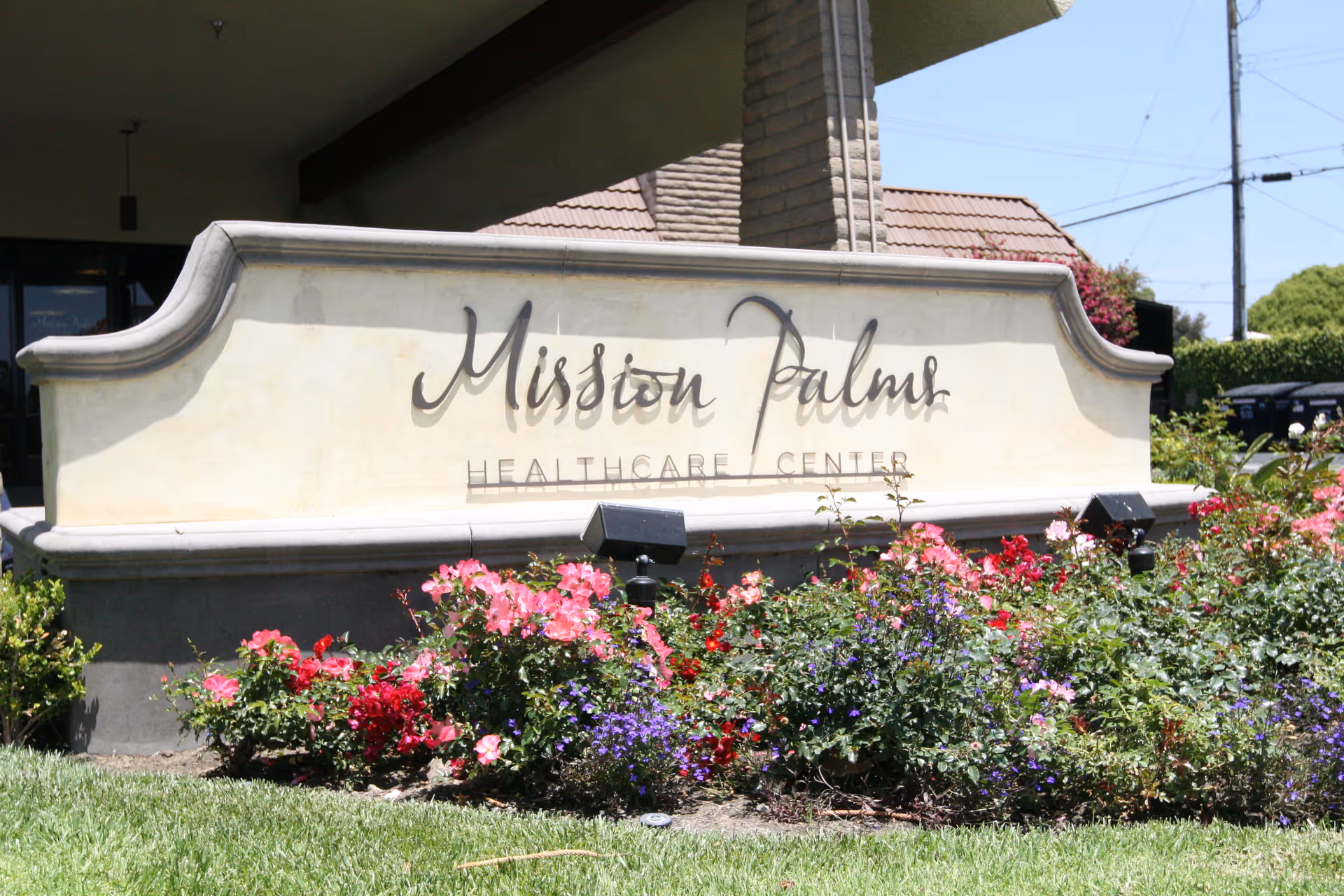 Entrance sign that reads "Mission Palms Healthcare Center" set behind a flowerbed and landscaping.