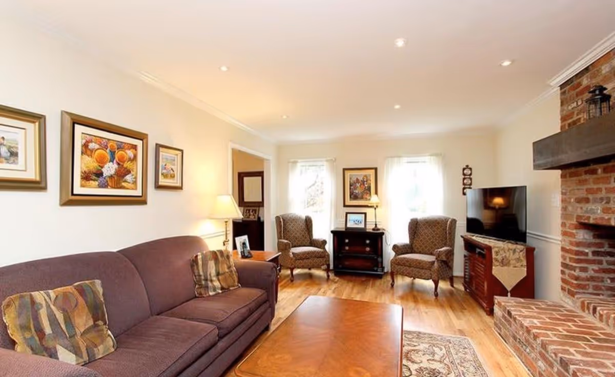 Well-lit living room with a sofa, two armchairs, coffee table, TV cabinet and a brick fireplace.