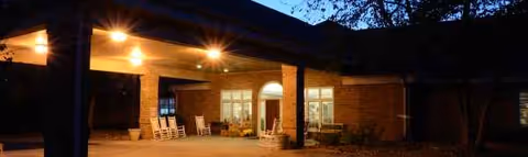 Evening exterior view of Maples at Austin Place entrance with brick facade and outdoor seating.