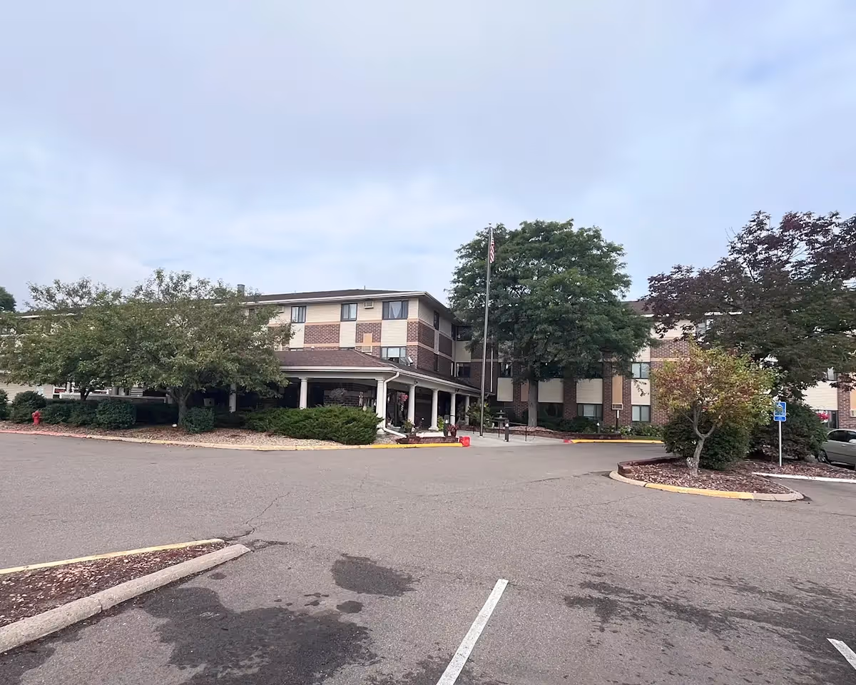 Exterior view of Oak Ridge Manor, a brick senior living facility with a covered entrance, flagpole, and surrounding trees in a parking lot setting.