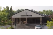 Front entrance of Saint John XXIII Home with a covered portico, sign bearing a cross, landscaping, and a parked car.