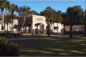 Exterior view of Avante at Ocala facility showing a large building with an arched entrance surrounded by palm trees and a well-maintained lawn under a clear sky.
