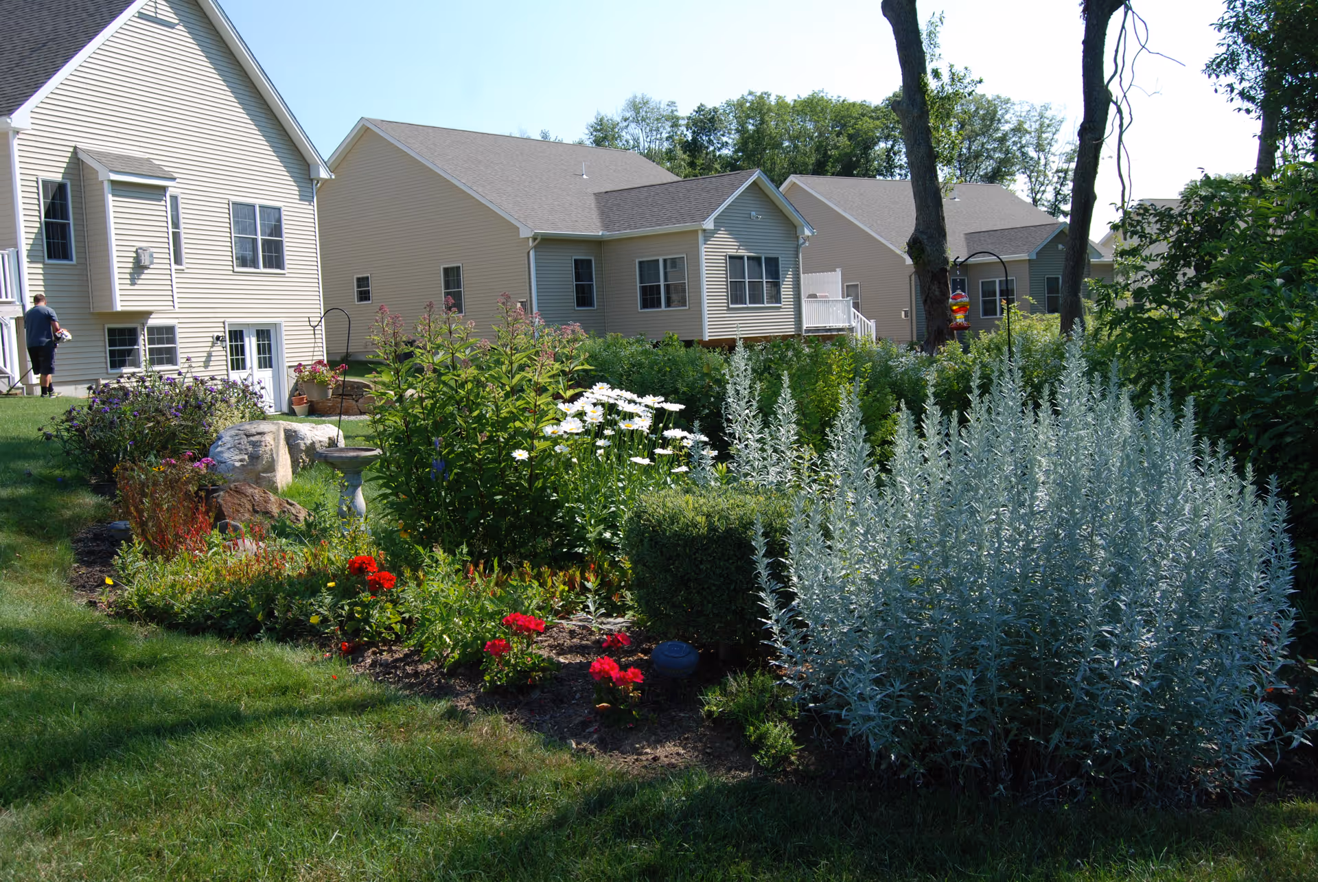 Colorful landscaped garden and lawn with flowers and shrubs in front of beige residential buildings.
