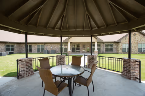 Covered outdoor patio with a round glass table and wicker chairs overlooking a lawn.