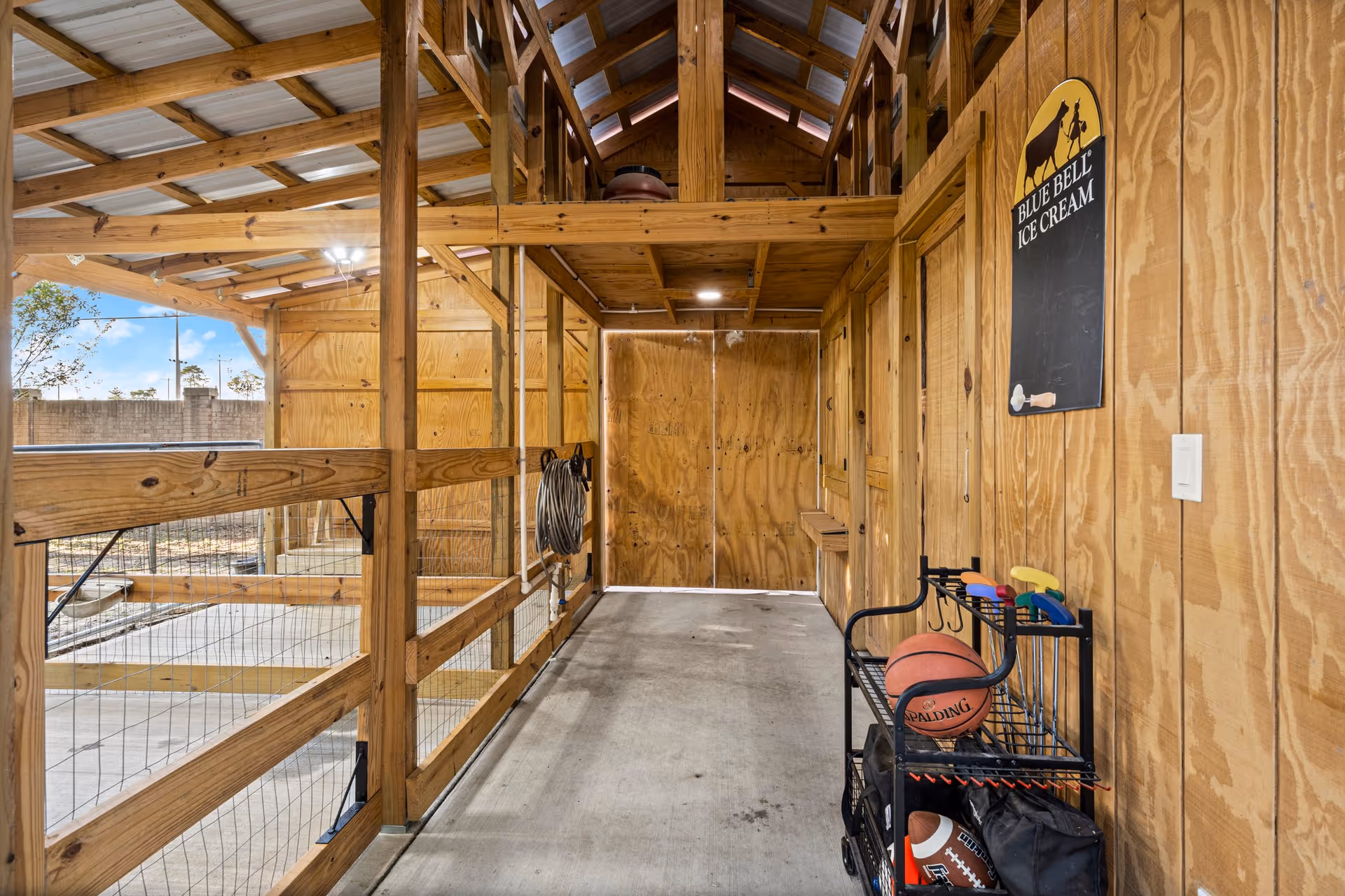 Covered wooden corridor with wire-railed railing and a cart of sports balls under a metal roof.