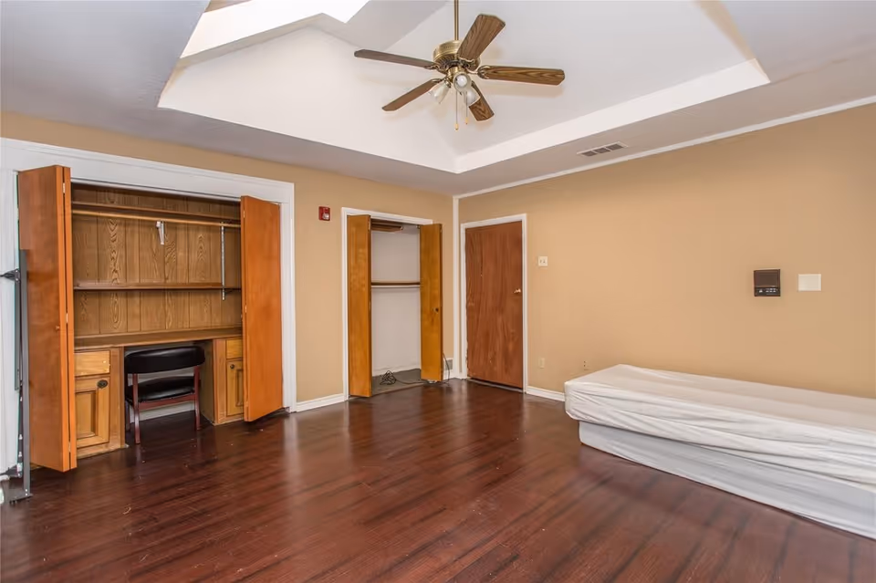 Empty bedroom with hardwood floors, a built-in desk/closet, ceiling fan, and a single mattress against the wall.