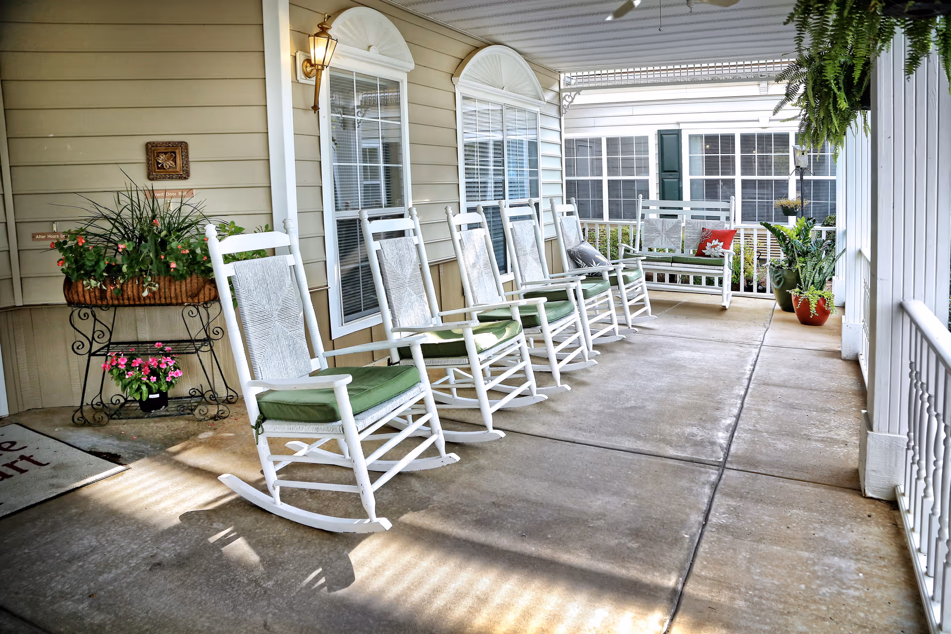 Covered porch with a row of white rocking chairs, potted plants, and a bench.