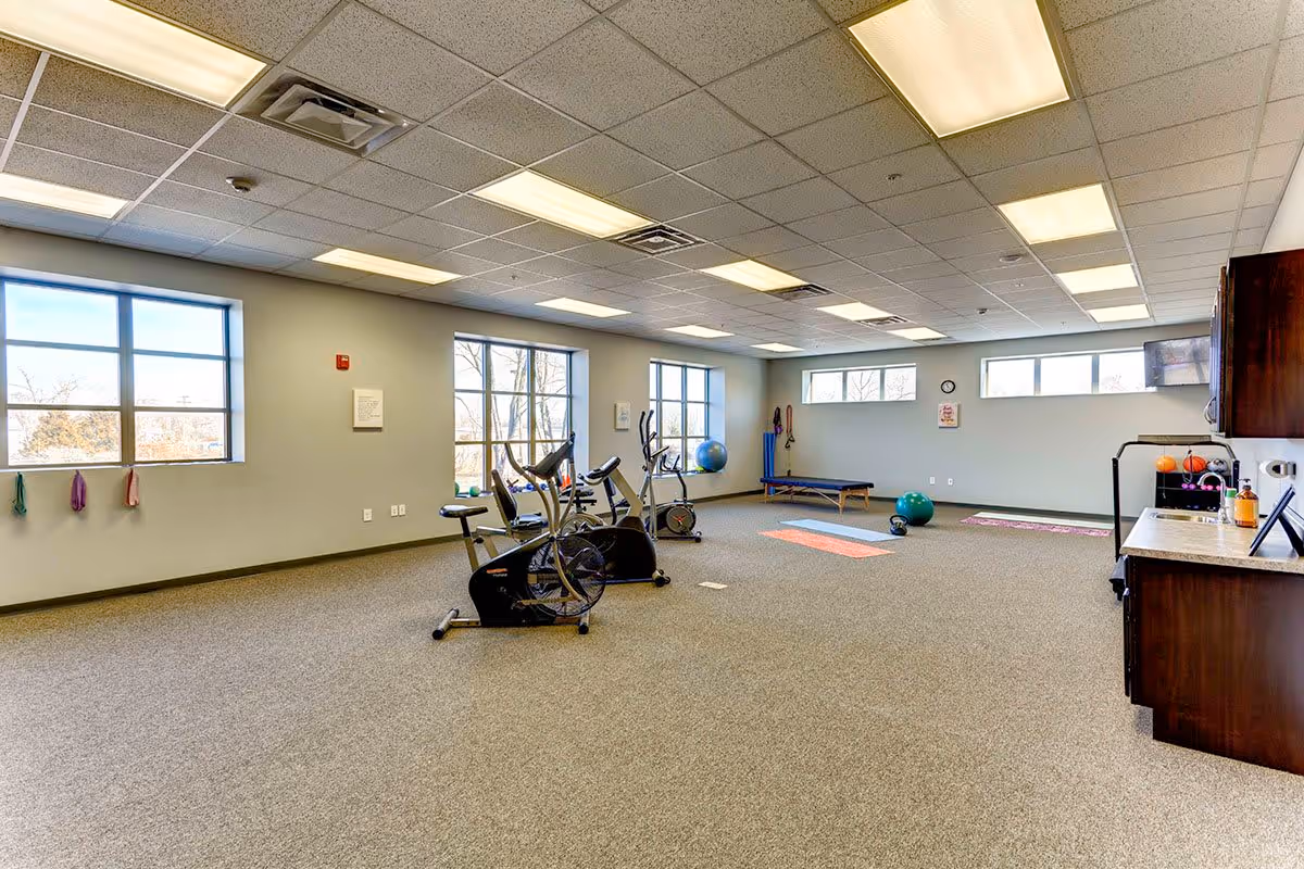 Large exercise room with stationary bikes, yoga mats, exercise balls and cabinets in a senior living facility.