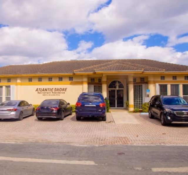 Front exterior of the Atlantic Shore Retirement Residence building with entrance and several parked cars.