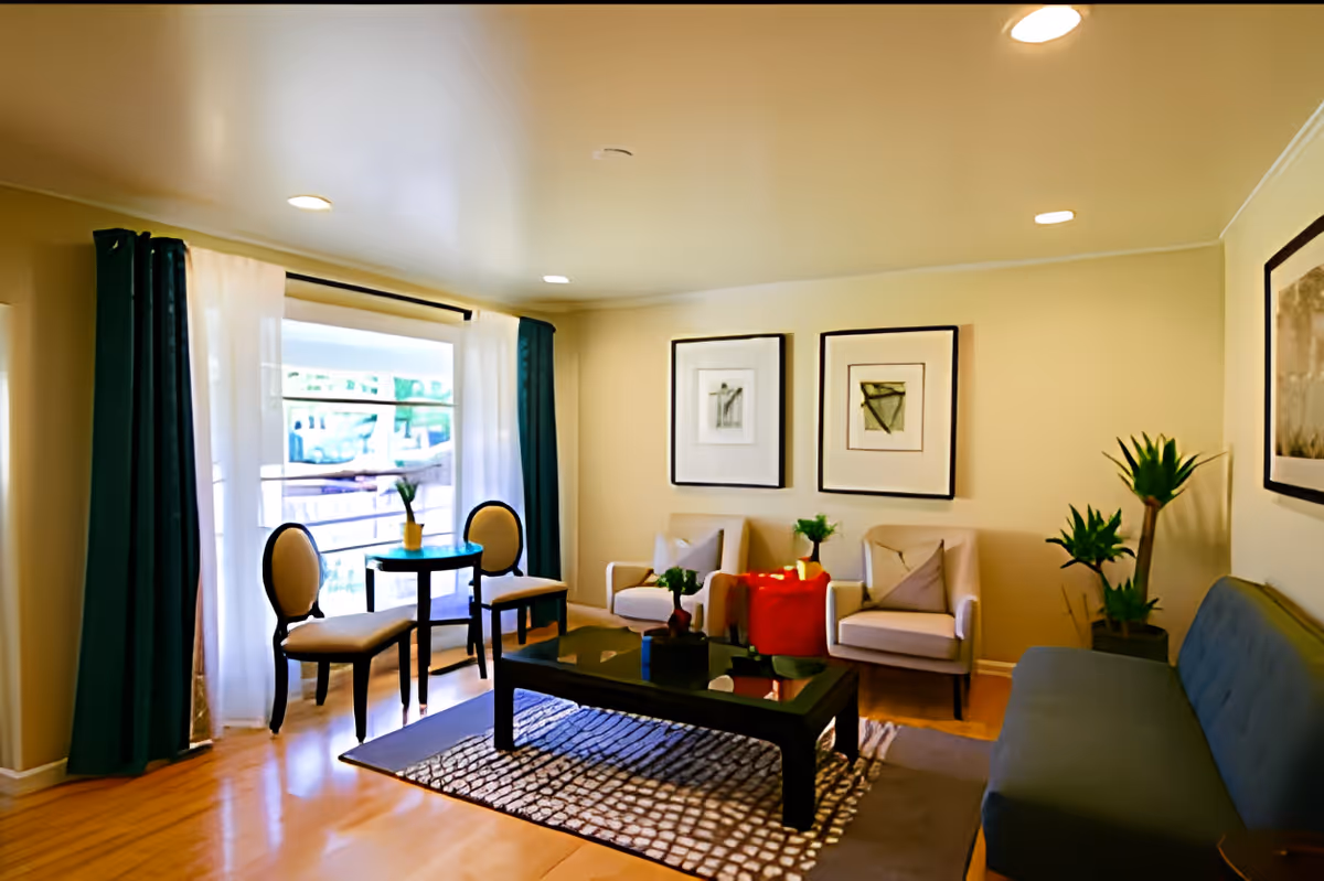 Bright furnished living room with armchairs, a sofa, coffee table, rug, framed artwork and a large curtained window.