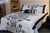 A neatly made bed with black-and-white floral patterned bedding and a striped bolster in a cozy bedroom with built-in shelving.
