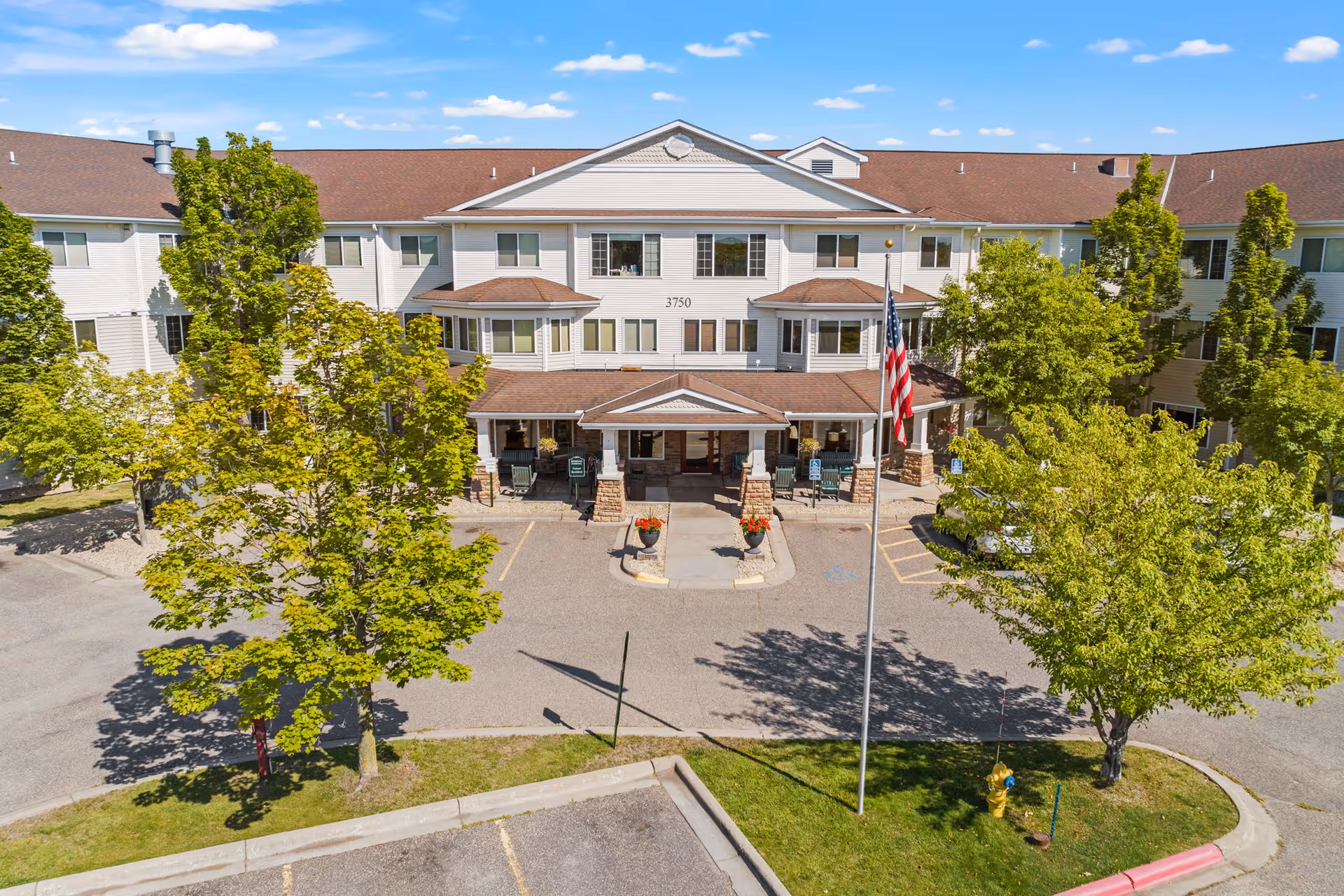 Exterior view of a senior living facility's front entrance with parking and trees.