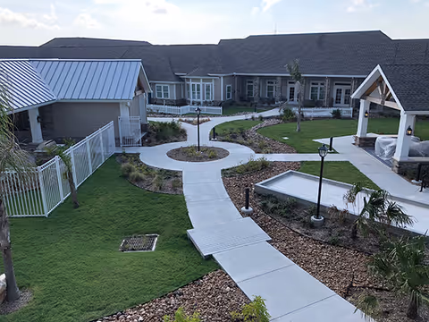 Landscaped courtyard with concrete walkways, lawns, lamp posts, a pavilion and surrounding single-story senior living buildings.