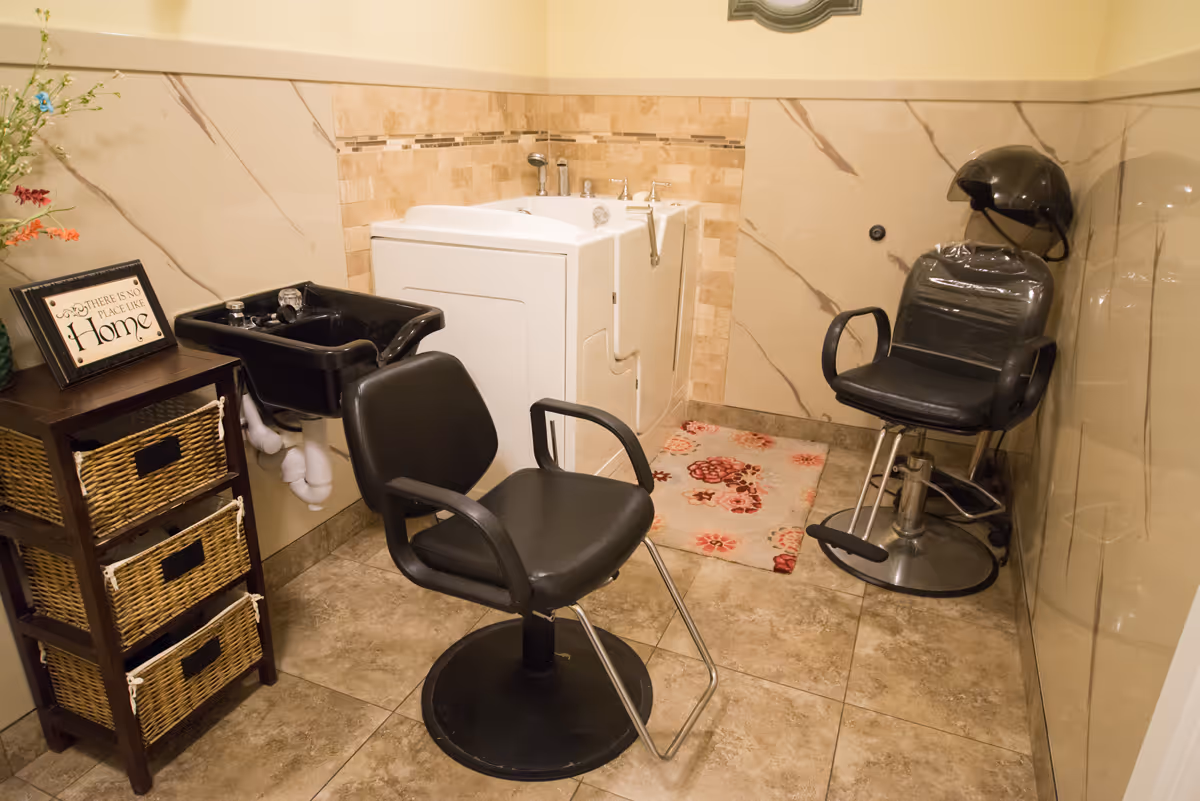 Small salon-style room with two black styling chairs, a shampoo sink, and a walk-in tub against tiled walls.
