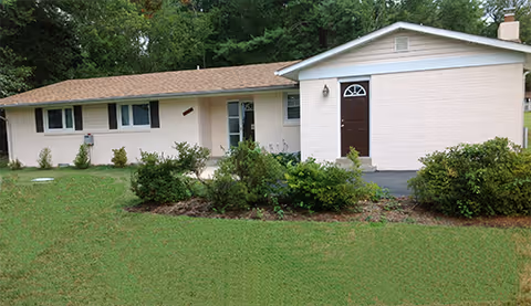 Single-story beige building exterior with shrubs and a dark front door.