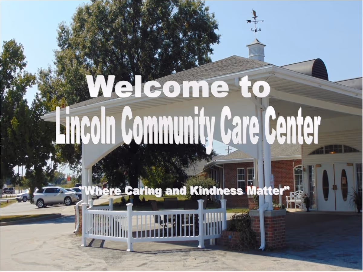 Entrance of Lincoln Community Care Center with a covered driveway, white railing, brick pillars, and a weather vane on the roof. Trees and parked cars are visible in the background. Text overlay reads 'Welcome to Lincoln Community Care Center' and 'Where Caring and Kindness Matter'.