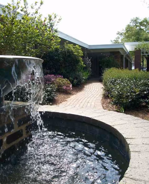 Exterior view of Naomi Heights Nursing and Rehabilitation Center with a fountain and brick path.