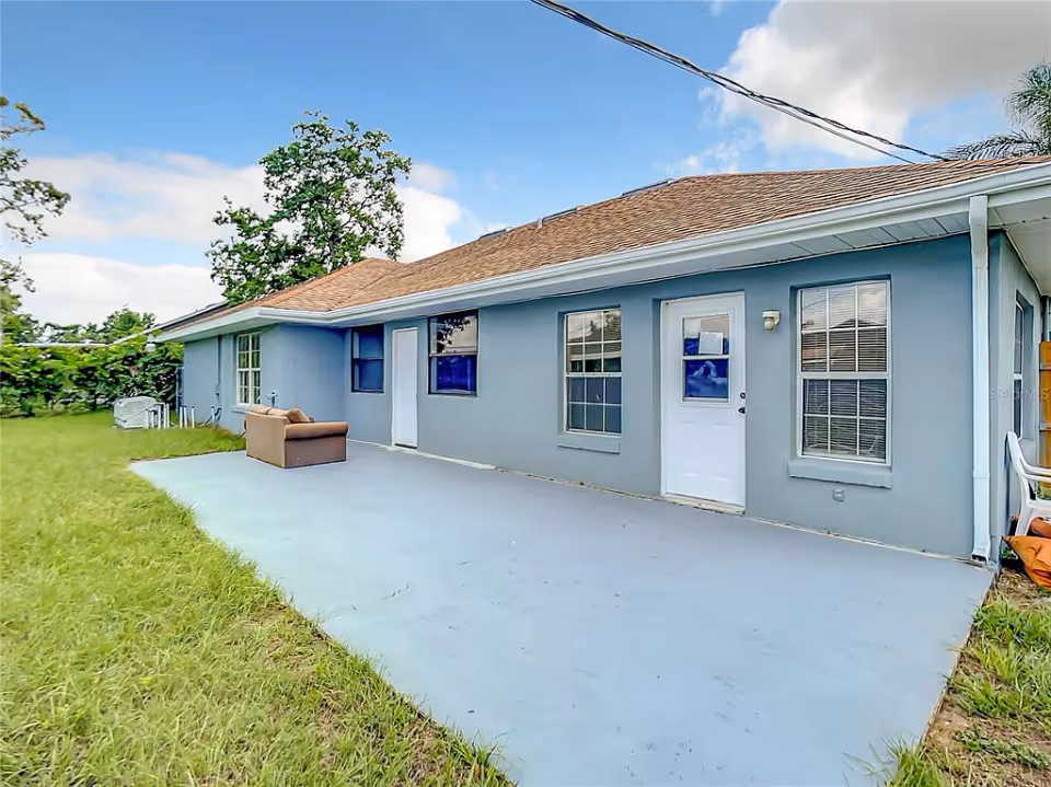 Single-story blue house exterior with a concrete patio, lawn, and a couch placed on the patio.