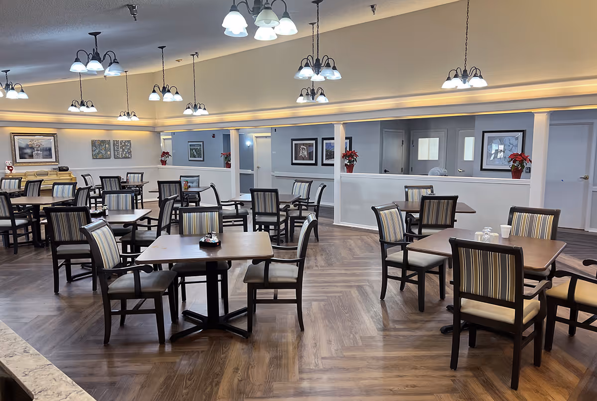 Spacious dining area with multiple wooden tables and striped upholstered chairs beneath hanging chandeliers.