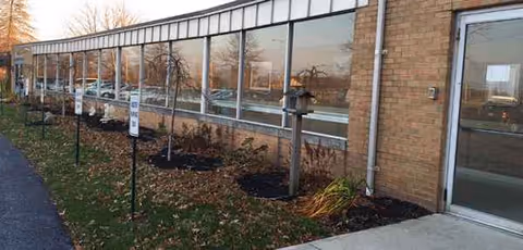 Brick senior living facility exterior with large windows, a glass door, and landscaped garden beds.