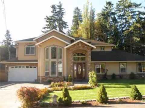 Front view of a tan, two-story senior living facility with curved window and driveway.