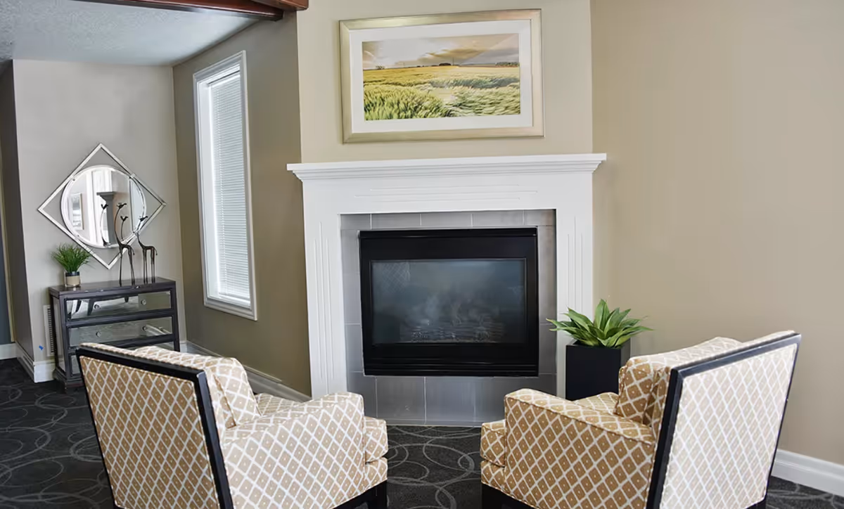 Two patterned armchairs face a fireplace in a cozy seating area with a side table, mirror, and wall art.