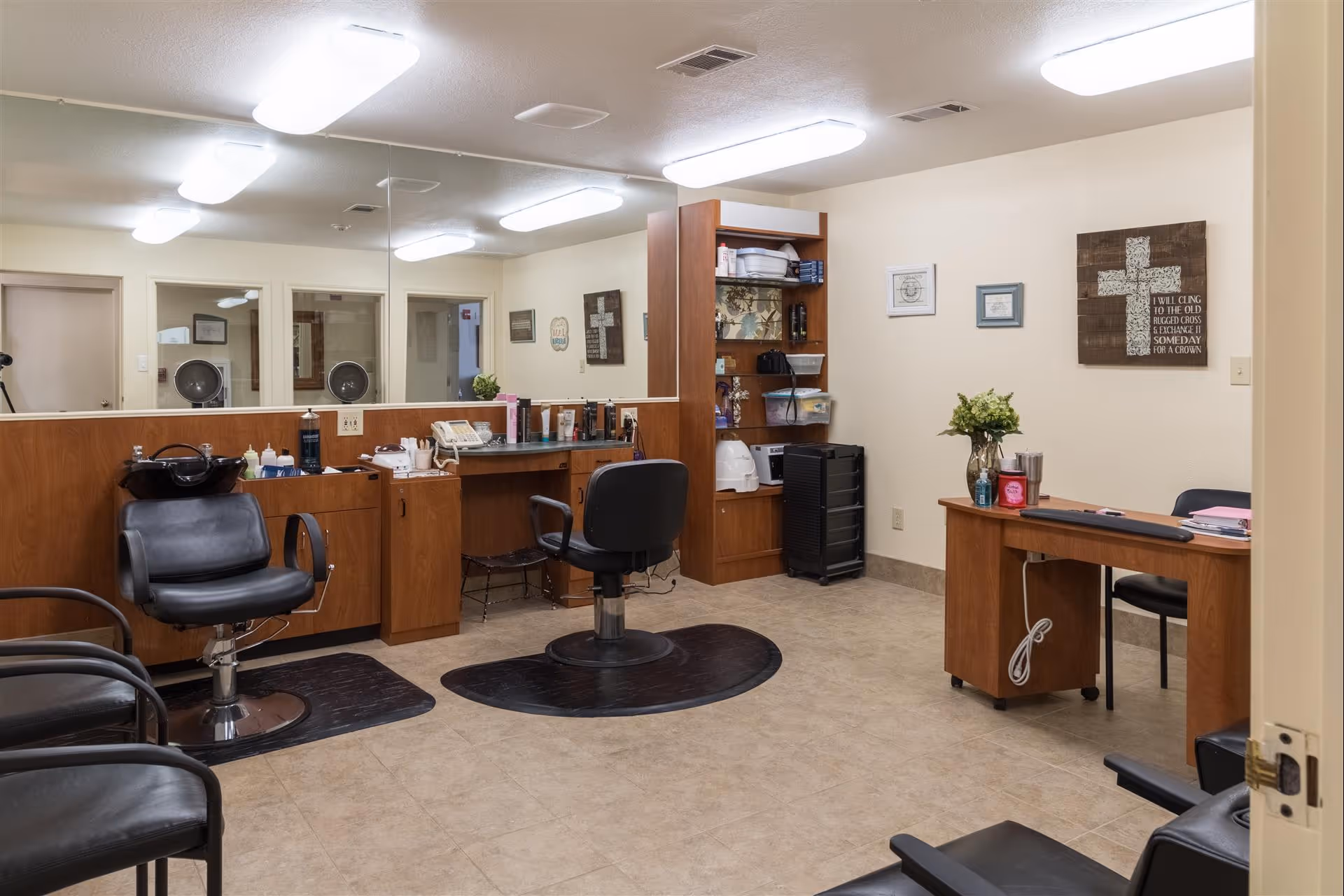 Interior salon room with styling chairs, large mirror, workstations and a small desk.