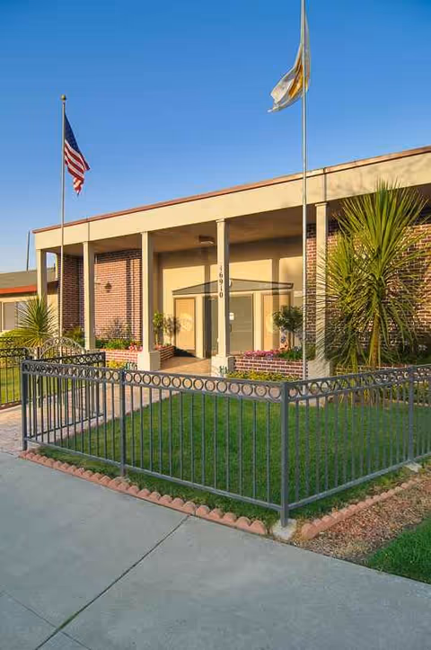 Front view of a senior living facility with flags, brick walls, and a gated lawn.