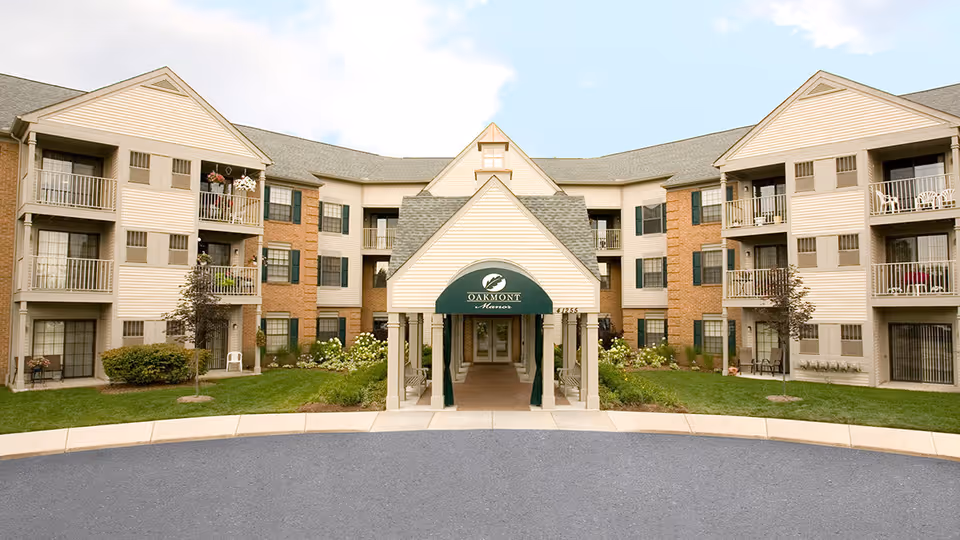 Front exterior view of Oakmont Manor Senior Community building with a covered entrance, multiple balconies, and landscaped greenery.