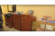 Interior room showing a wooden salon/storage station with a mirror, assorted supplies on trays, and chairs.
