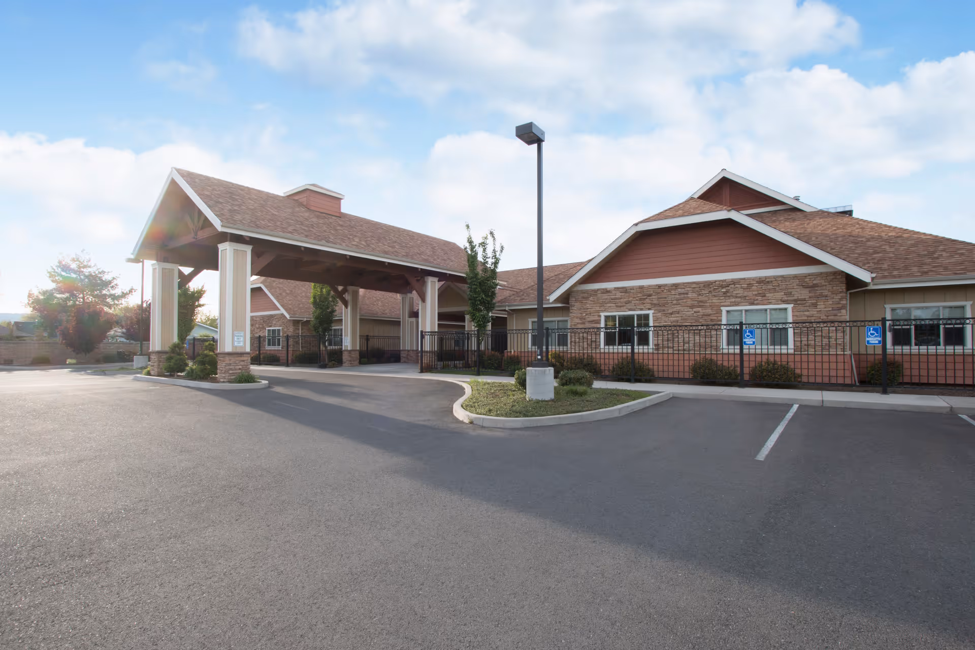 Front entrance and parking lot of a single-story senior living facility with a covered porte-cochere and landscaped islands.