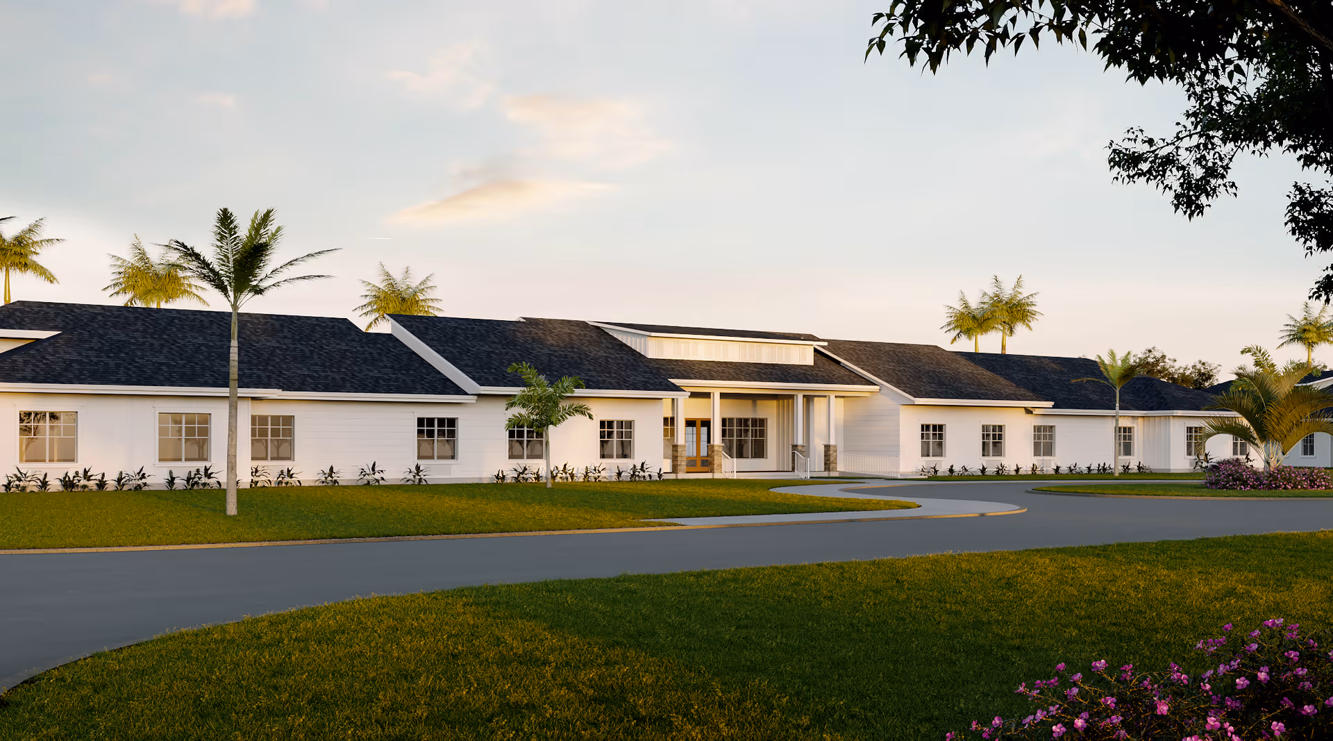 Exterior view of a single-story senior living facility building with white siding, dark shingled roofs, and multiple windows. The building is surrounded by green grass, palm trees, and landscaped flower beds under a partly cloudy sky.