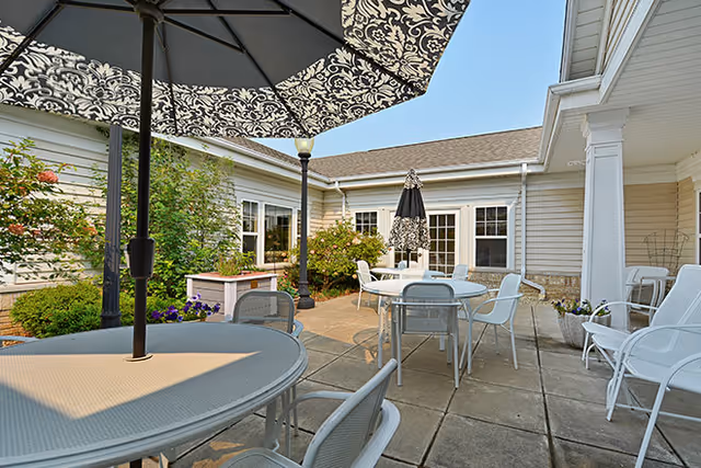 Sunlit outdoor courtyard patio with tables, chairs, umbrellas and surrounding single-story building.