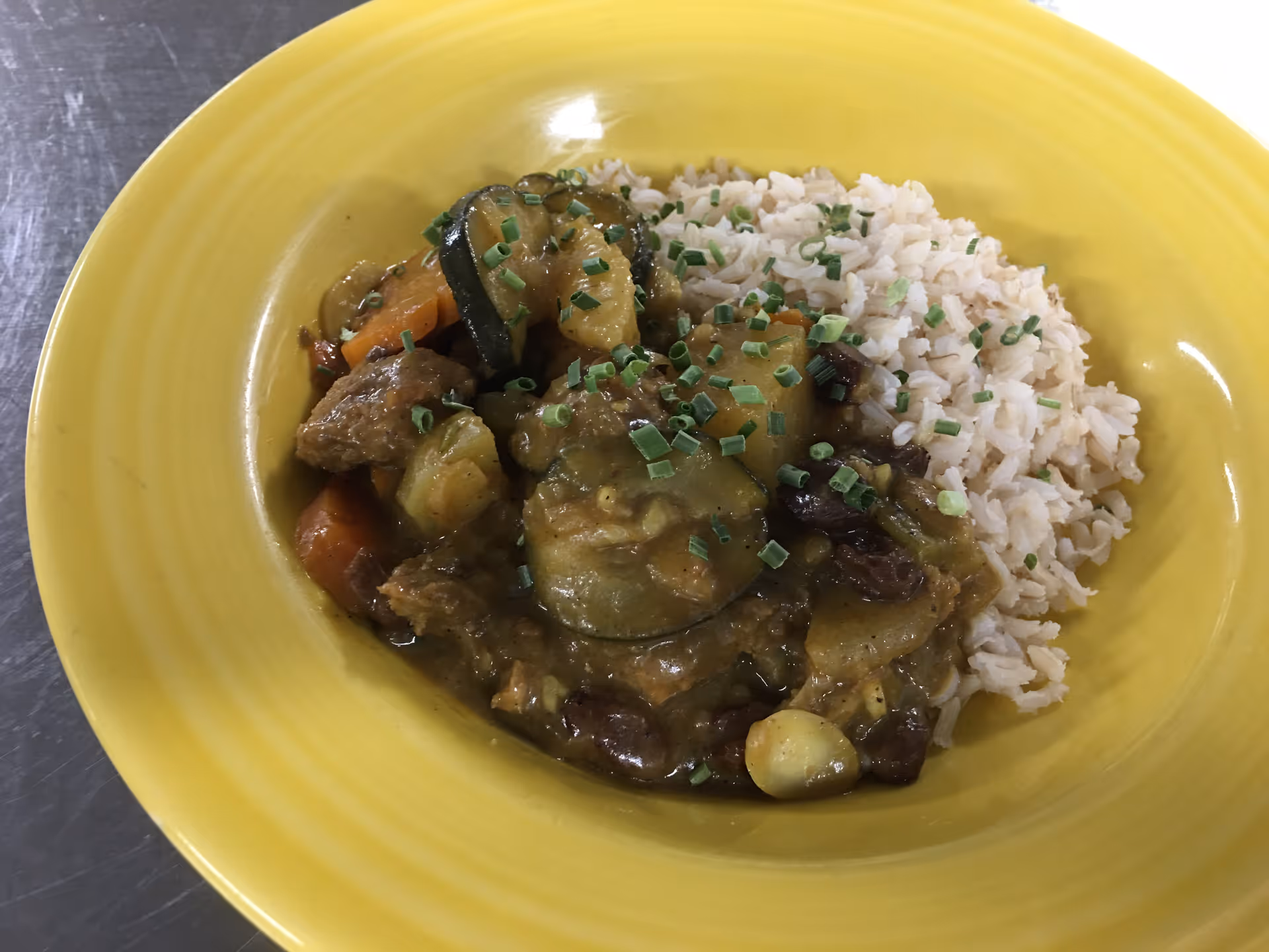 Bowl of rice and vegetable curry garnished with chopped chives on a yellow plate.
