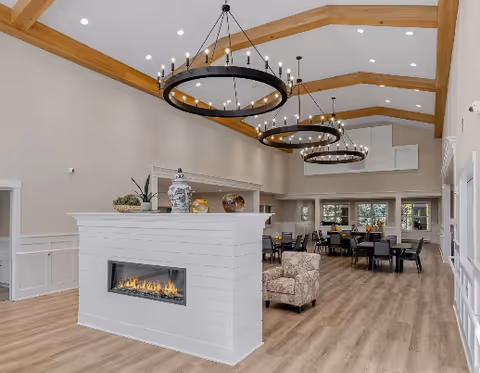 Spacious indoor common area with a white fireplace, exposed wooden beams, and circular chandeliers.