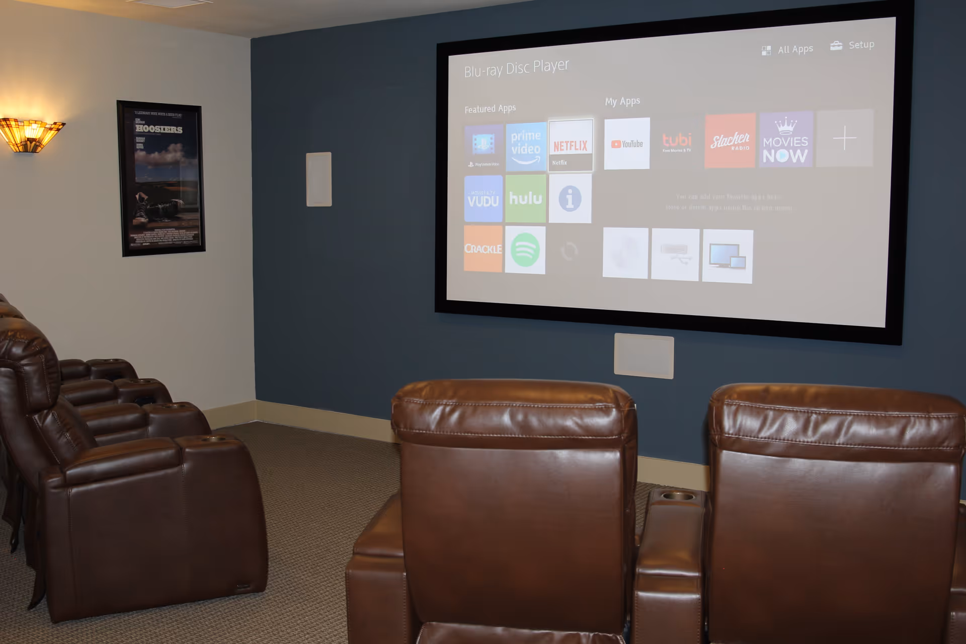 Small screening room with rows of brown leather recliners facing a large wall-mounted projection screen showing streaming app icons.