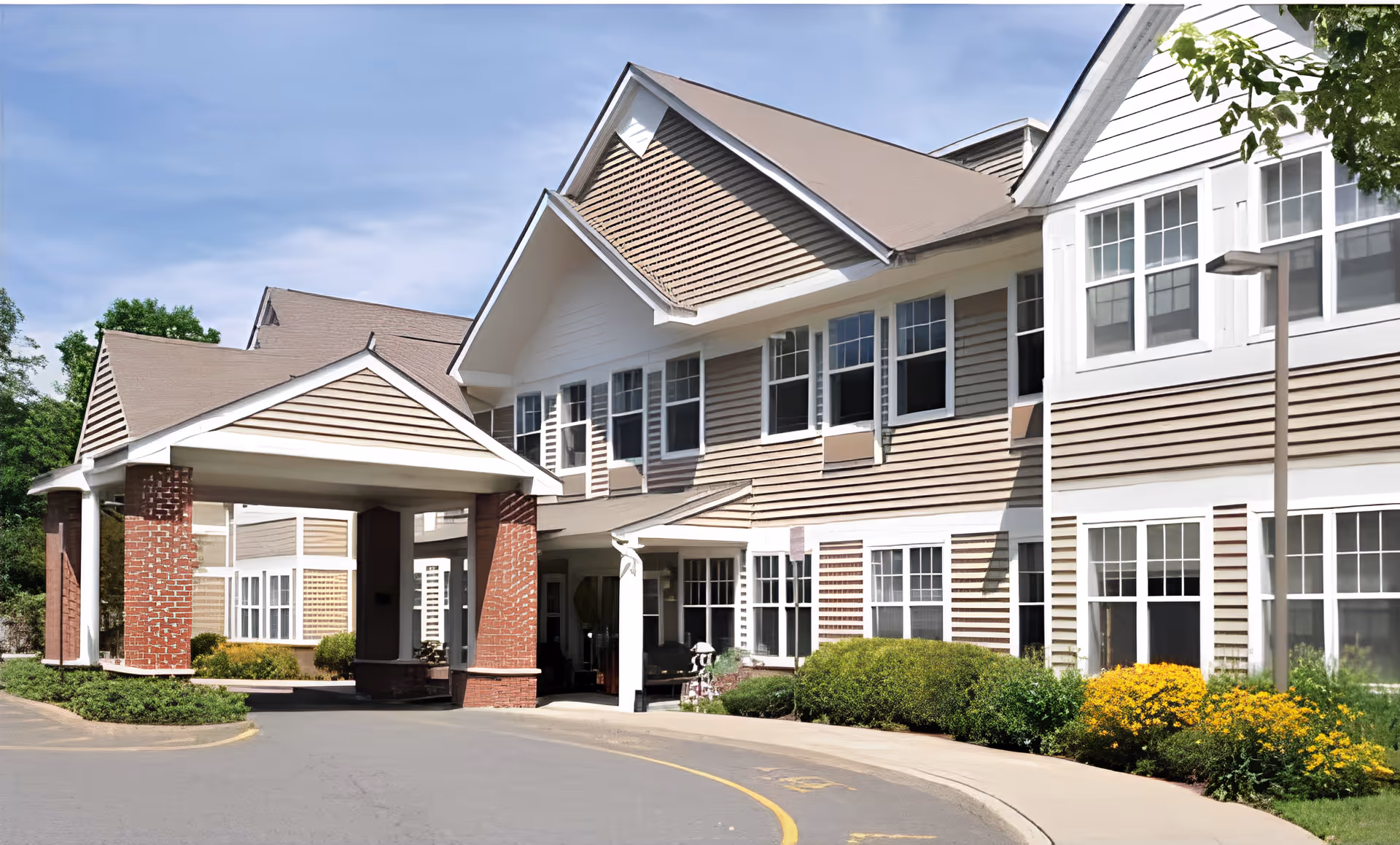 Front entrance of a two-story senior living building with a covered porte-cochere and landscaped driveway.
