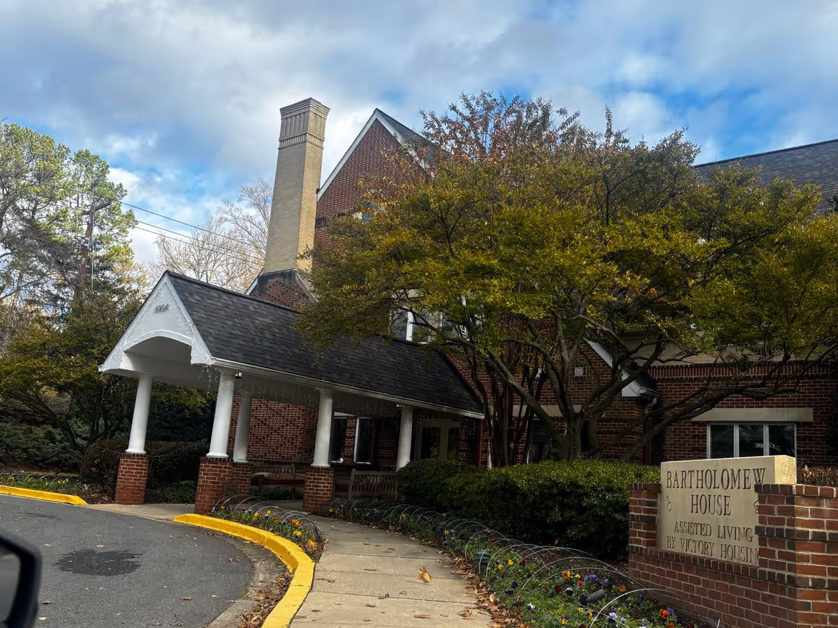 Front entrance of Bartholomew House assisted living building with a covered portico, sign, and landscaped walkway.