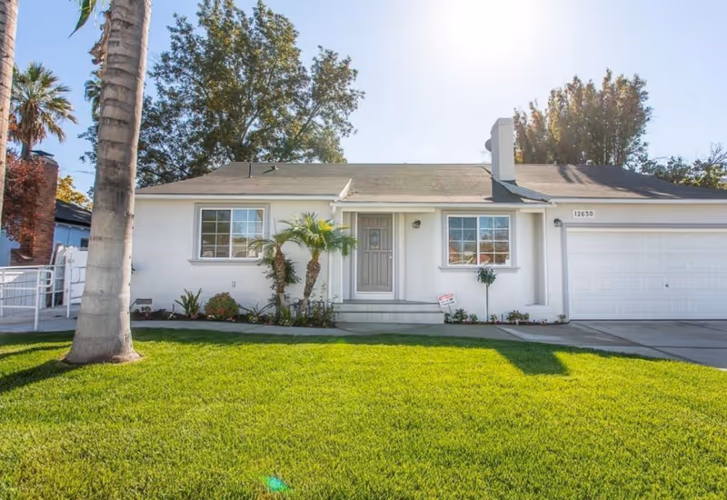 Single-story white building with a two-car garage, front yard, and palm trees.