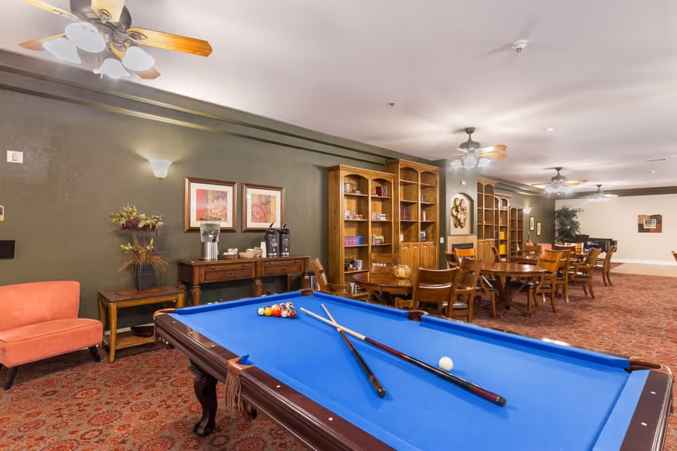 Interior common room with a blue pool table, seating, bookshelves and dining tables.