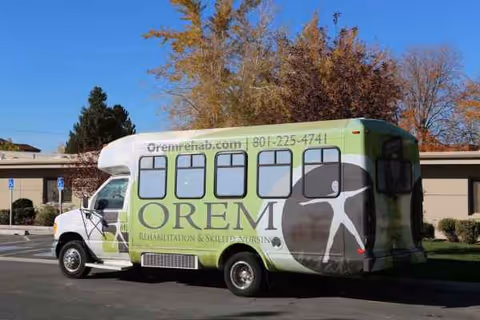 Green and white OREM Rehabilitation shuttle bus parked in a lot beside a building.