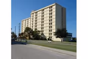 Tall beige senior living facility viewed from street with lawn and trees.
