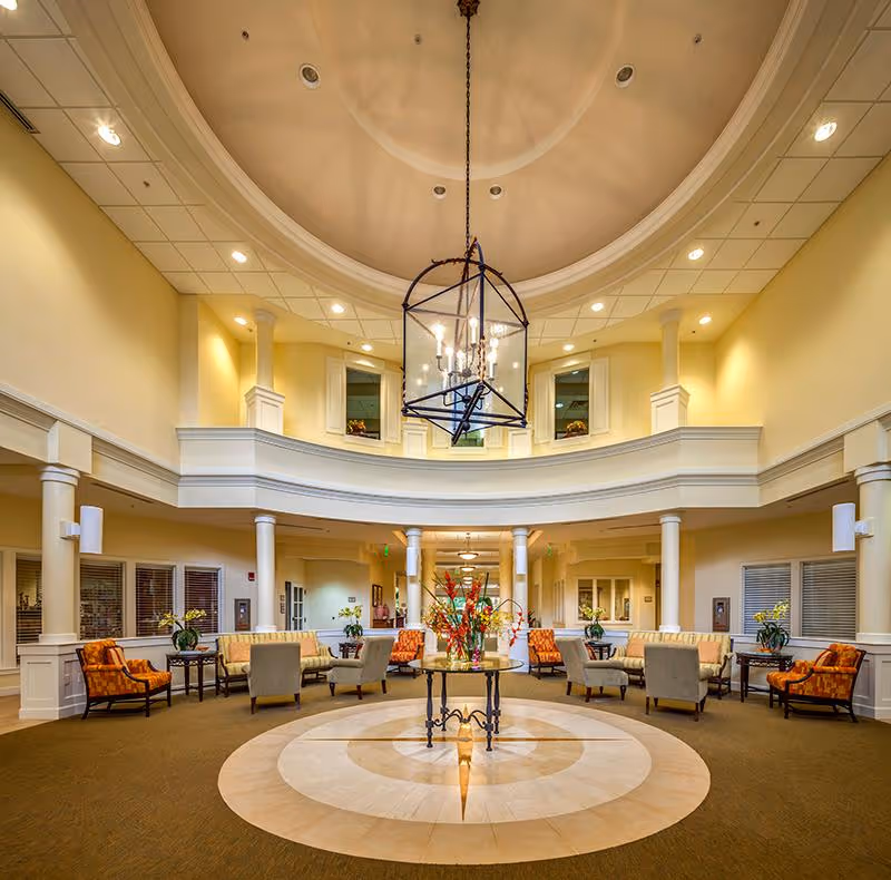 Spacious two-story lobby with a central chandelier, circular tiled floor medallion and multiple seating areas surrounded by columns.